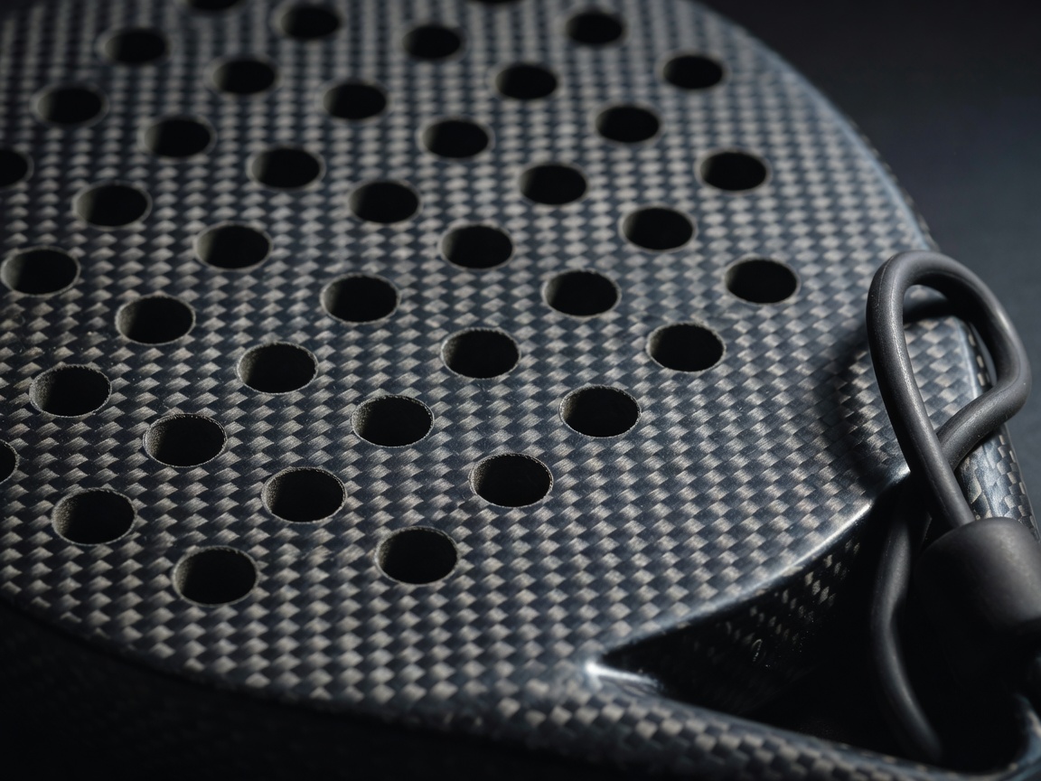 Close-up of the perforated face of a carbon fibre padel racket showing surface texture